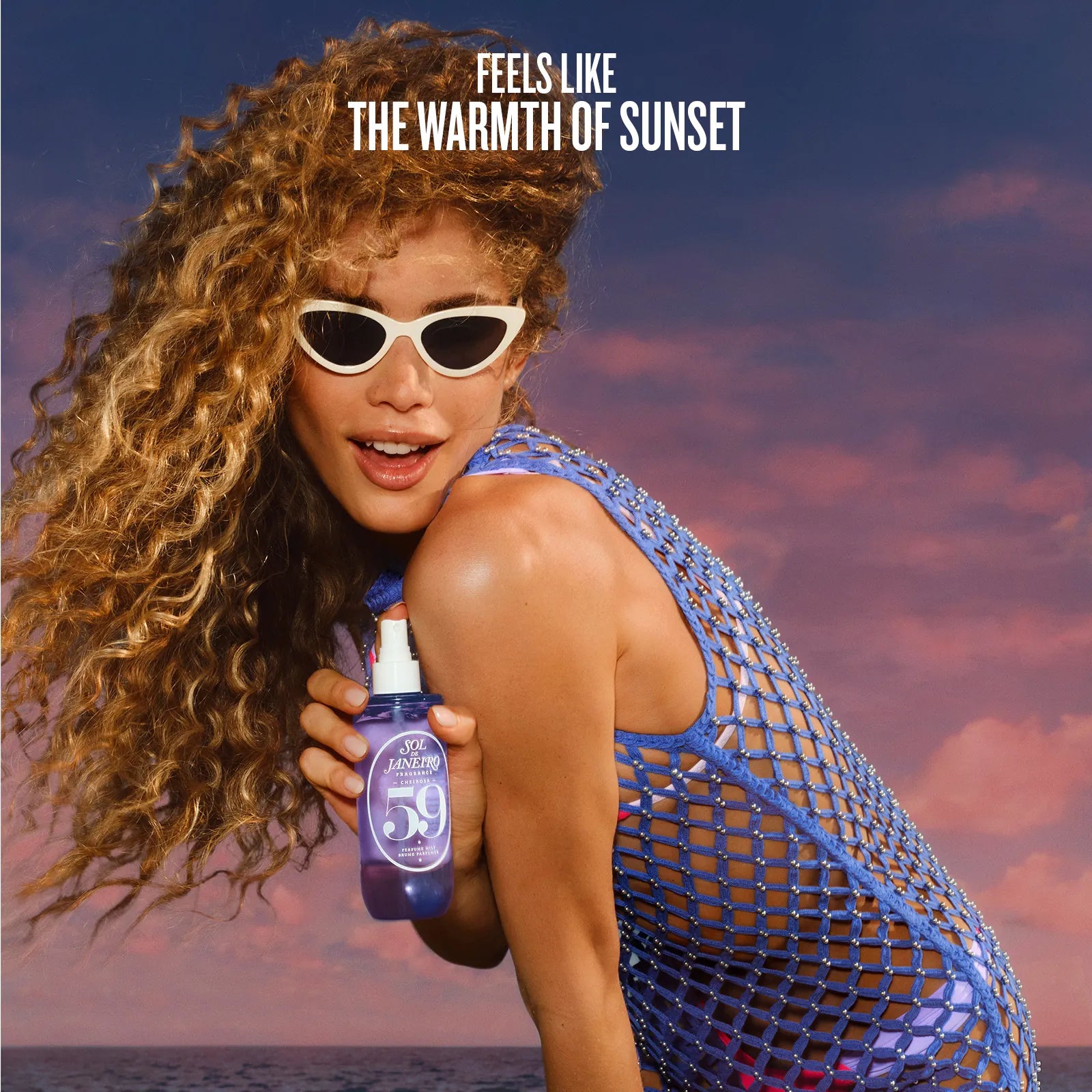 Woman holding a bottle of sunscreen with a sunset background