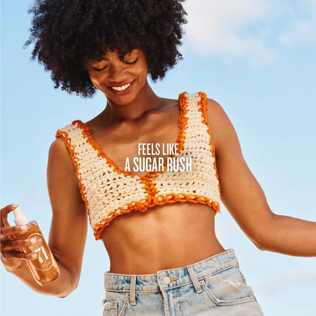 Woman wearing a crochet top with 'Feels Like a Sugar Rush' text, holding a bottle against a clear blue sky.