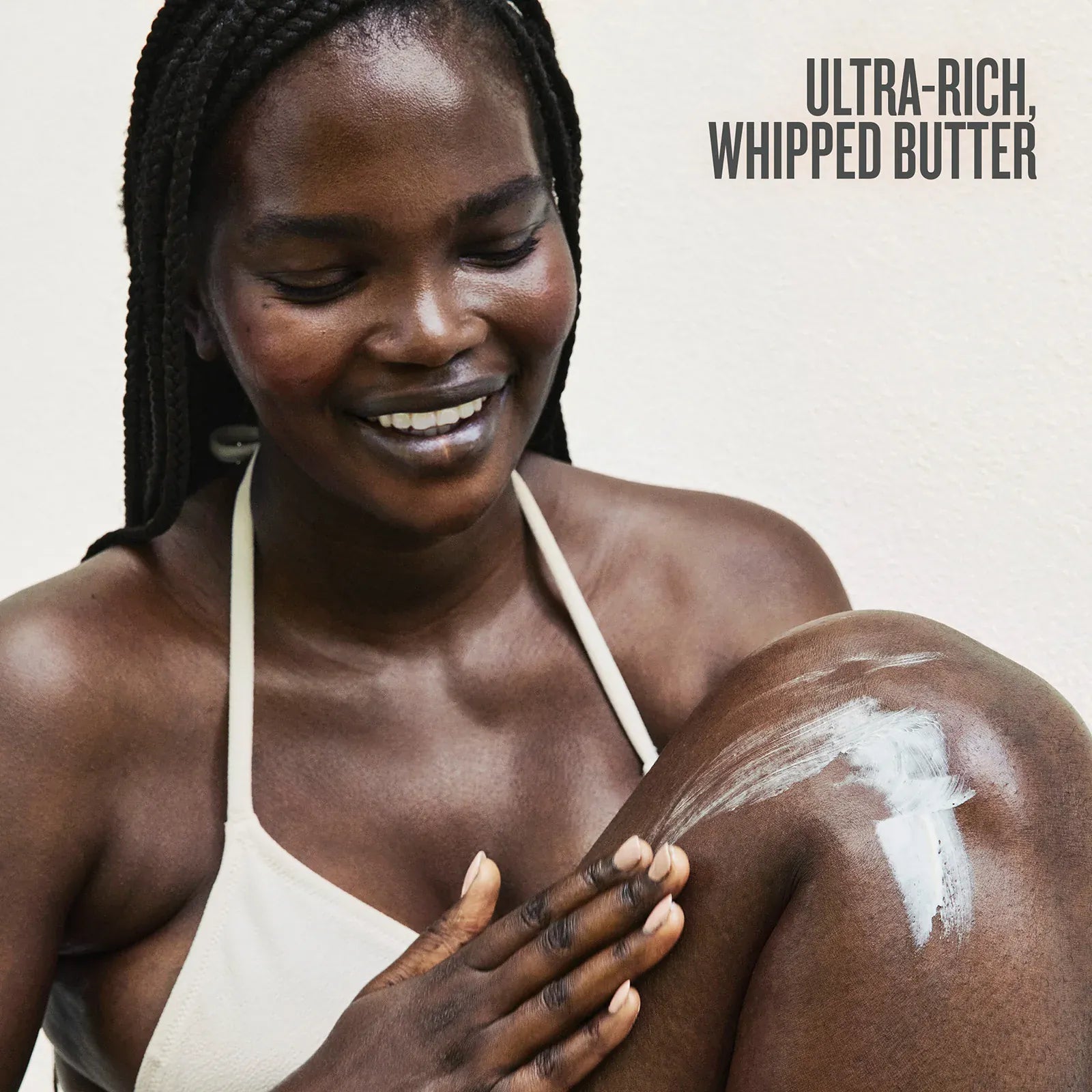 Woman applying ultra-rich whipped butter to her arm with a neutral background