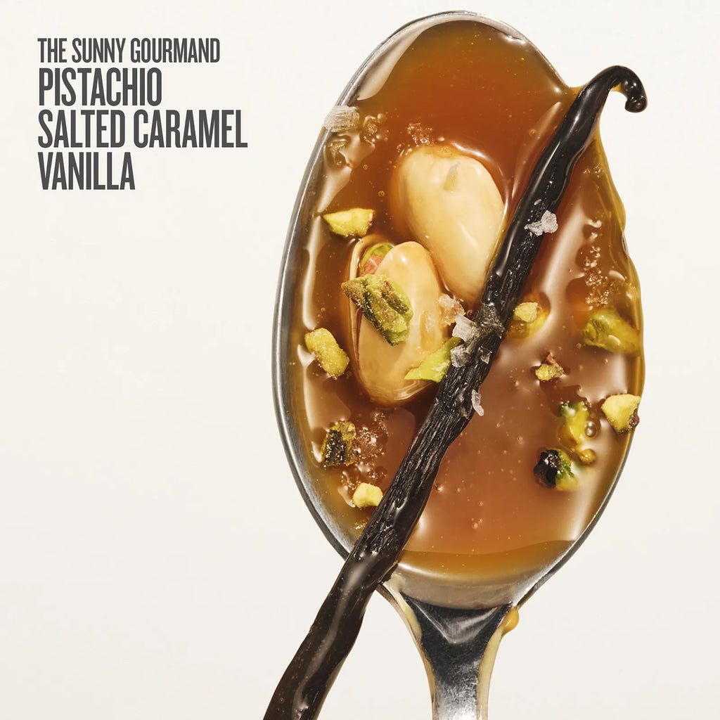 Spoon with dessert featuring salted caramel, vanilla beans, and pistachios on a white background.