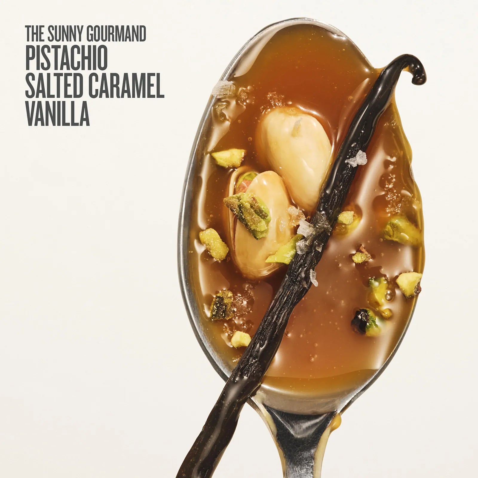 Spoon with salted caramel sauce, vanilla beans, and pistachios on a white background.