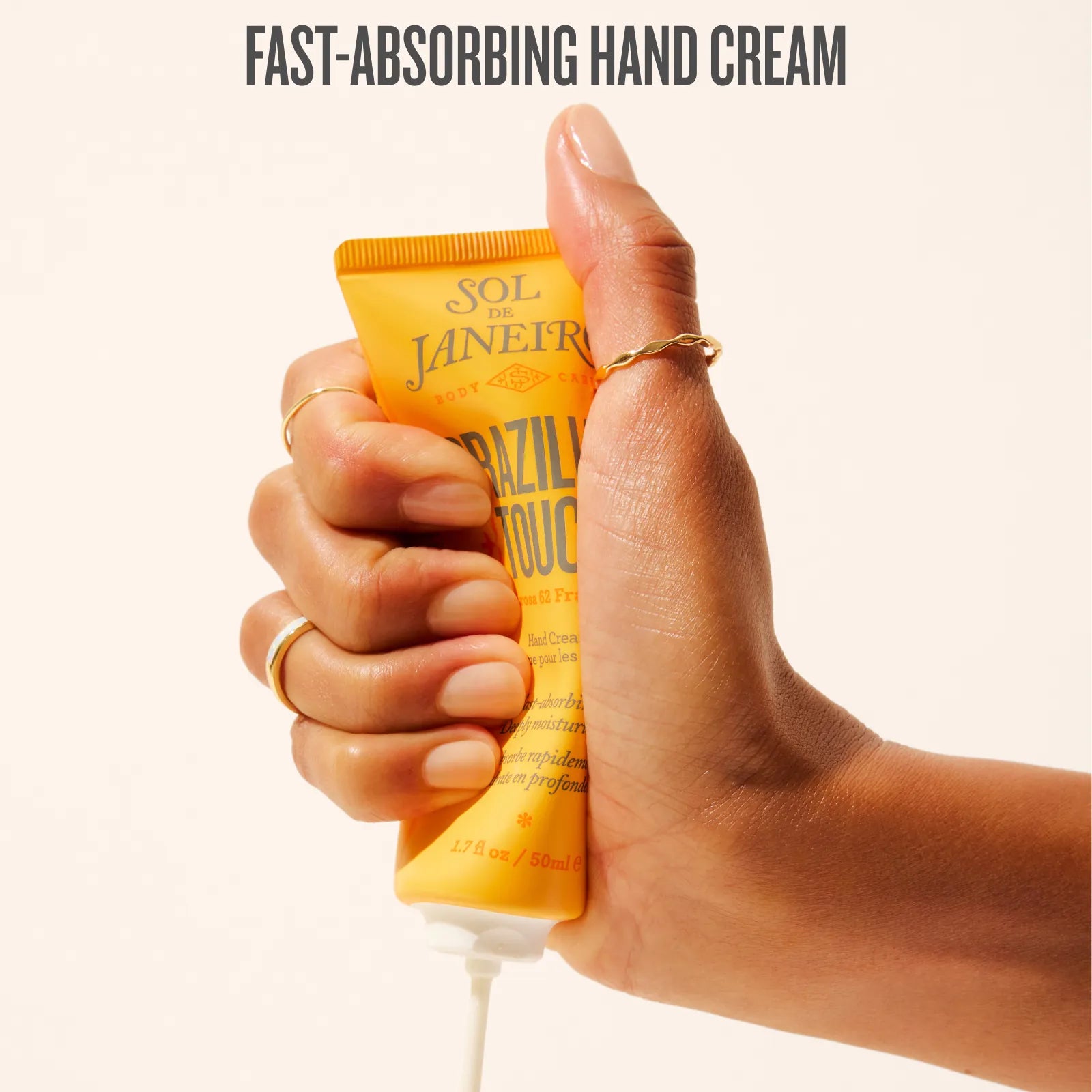 Hand holding a tube of Sol de Janeiro hand cream with text 'Fast-Absorbing Hand Cream'.